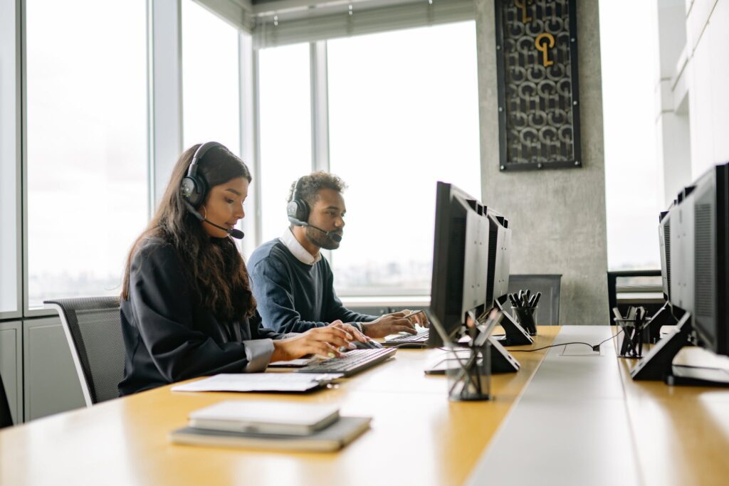 Two customer service representatives wearing headsets working at computers in a modern office.